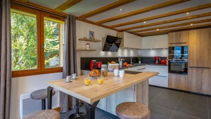 Una cocina moderna con una isla de madera, taburetes de bar y vistas a la vegetación exterior.