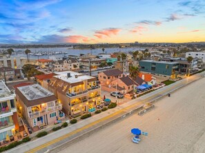 A coastal town with a beachfront hotel featuring balconies, outdoor seating, and a view of the sea.