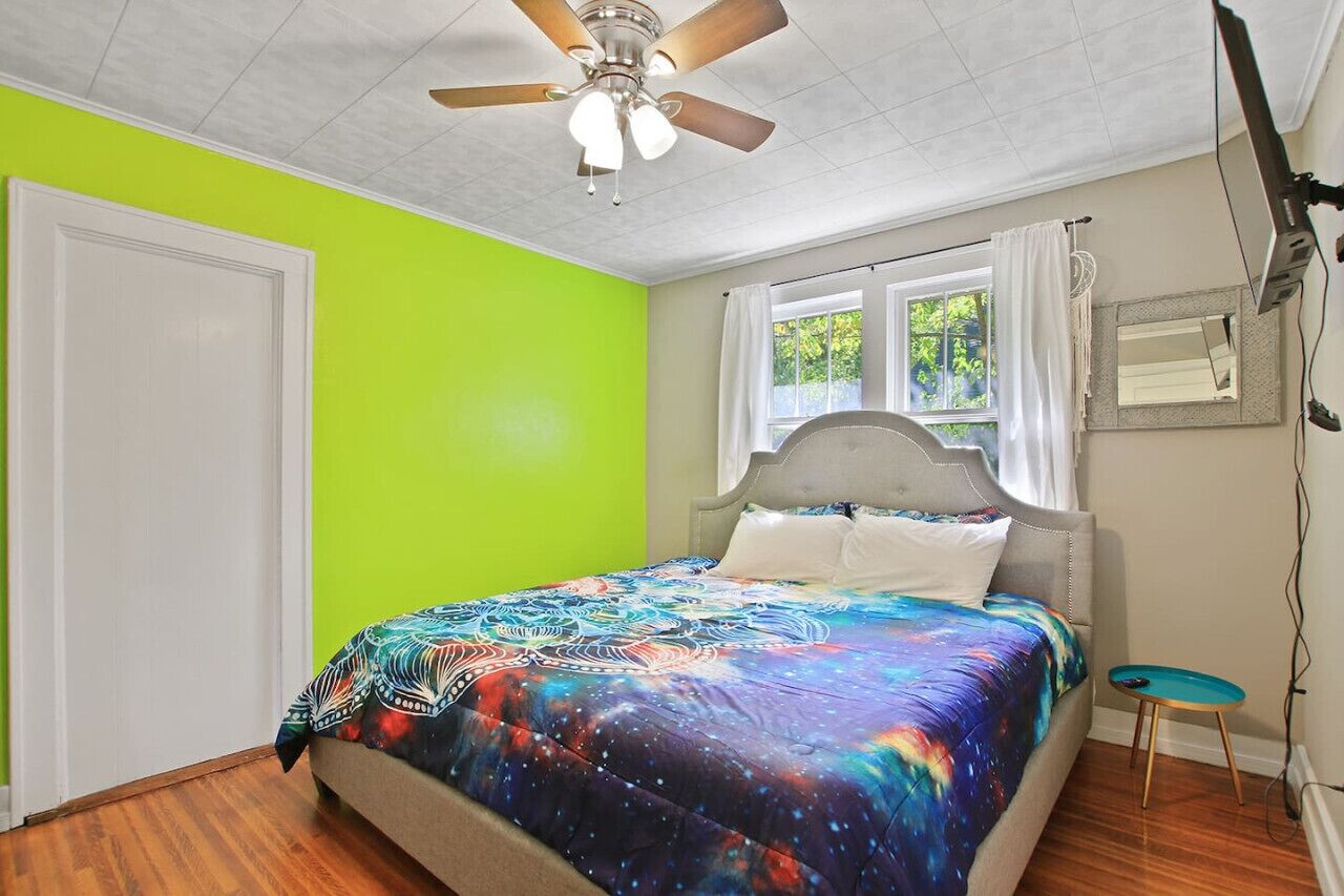A bedroom with a bed, a ceiling fan, a window with curtains, and a small table.