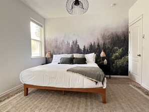 A bedroom with a large bed, a forest mural on the wall, a window, and a door. - Cl113 Moonstone Acre (Columbia Falls)