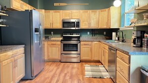 A kitchen with wooden cabinets, a stainless steel refrigerator, an oven, a microwave, and a coffee maker. - Cl113 Moonstone Acre (Columbia Falls)