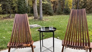 Two wooden Adirondack chairs with metal legs and a small round table with a glass and water bottle between them. - Cl113 Moonstone Acre (Columbia Falls)