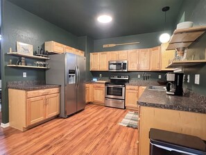 A kitchen with wooden cabinets, a stainless steel refrigerator, a microwave, an oven, and a coffee maker. - Cl113 Moonstone Acre (Columbia Falls)