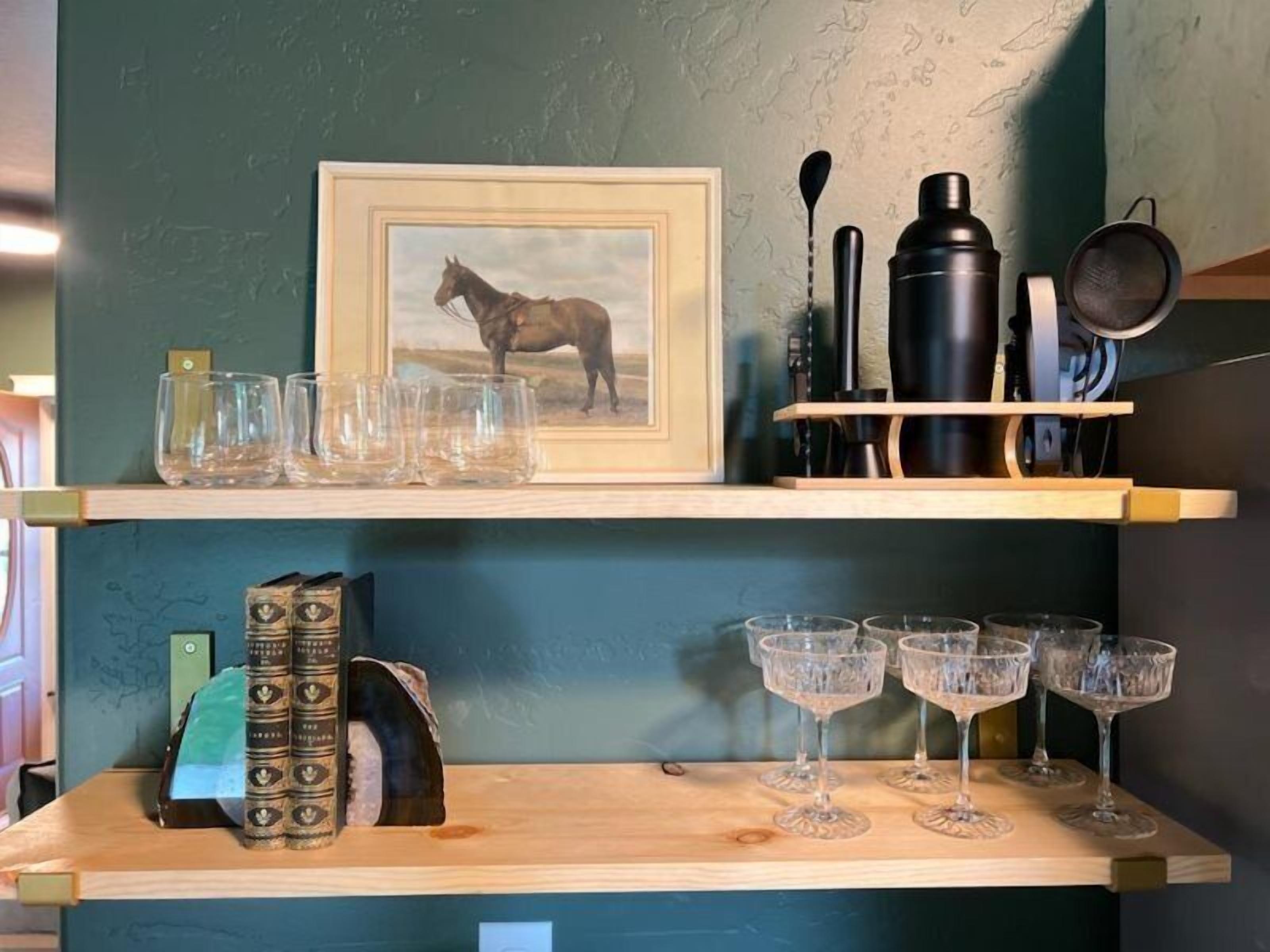 A shelf with a framed horse painting, a set of books, and a collection of glasses.