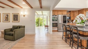 Uma sala de estar espaçosa com um sofá verde, vigas de madeira no teto e uma cozinha com armários de madeira e eletrodomésticos de aço inoxidável.
