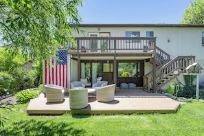 A two-story house with a deck, outdoor seating, and an American flag.