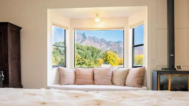 Quarto com uma cama grande, um assento junto à janela com almofadas e vista para as montanhas.