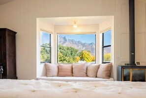 Une chambre avec un grand lit, un coin fenêtre agrémenté de coussins et une vue sur les montagnes.
