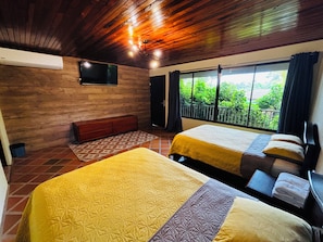 A room with two beds, a TV, and a window with a view of greenery.