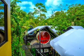 A treehouse structure with a red circular window, surrounded by lush greenery. - Arenal Backpackers Resort (La Fortuna)