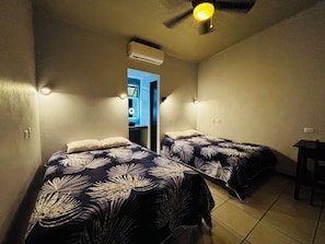 Une chambre avec deux lits, un climatiseur, un ventilateur de plafond et une petite table.
