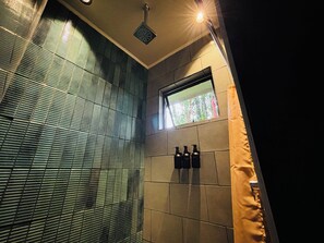 A bathroom with a shower, tiled walls, a window, and three bottles of shampoo.