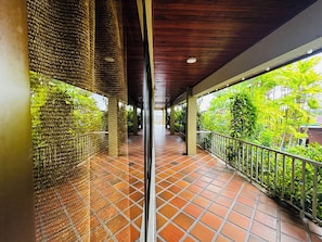 A covered corridor with tiled flooring, metal railings, and a view of lush greenery. - Arenal Backpackers Resort (La Fortuna)