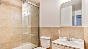 Ein Badezimmer mit Duschkabine, Toilette und Waschbecken mit Spiegel darüber.