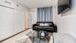 Ein Wohnzimmer mit einem schwarzen Ledersofa, einem Glastisch und einem grauen Vorhang.