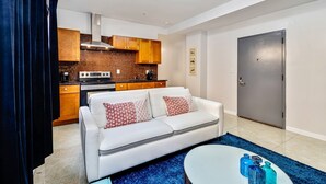 Uma sala de estar moderna com um sofá branco, uma mesa de centro redonda e uma área de cozinha com armários de madeira e um fogão.