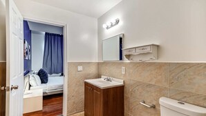 Casa de banho com toucador de madeira, lavatório, sanita e espelho com luzes.