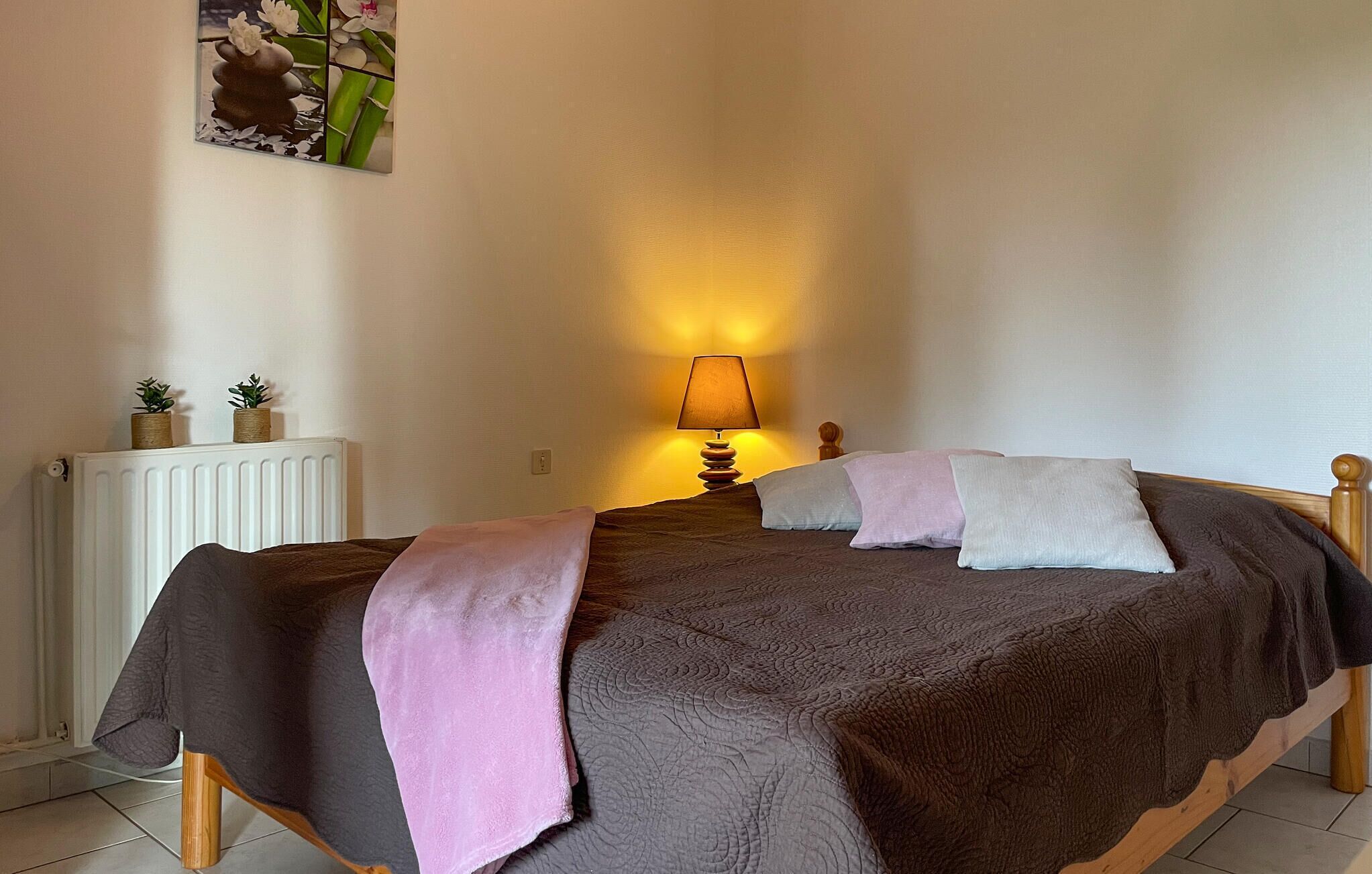 Een slaapkamer met een bed, een bedlampje, een radiator en twee kleine potplanten op de radiator.
