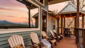 Eine Terrasse mit Adirondack-Stühlen, ein überdachter Bereich mit Lichterketten und Blick auf Berge.