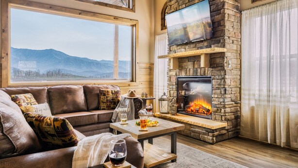 Ein gemütliches Wohnzimmer mit Kamin aus Naturstein, einem großen Fenster mit Bergblick und einer bequemen Sitzecke.