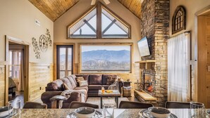 Ein gemütlicher Innenraum mit Kamin aus Stein, einem großen Fenster mit Bergblick, Holzboden und einem Essbereich mit Granit Arbeitsplatten.