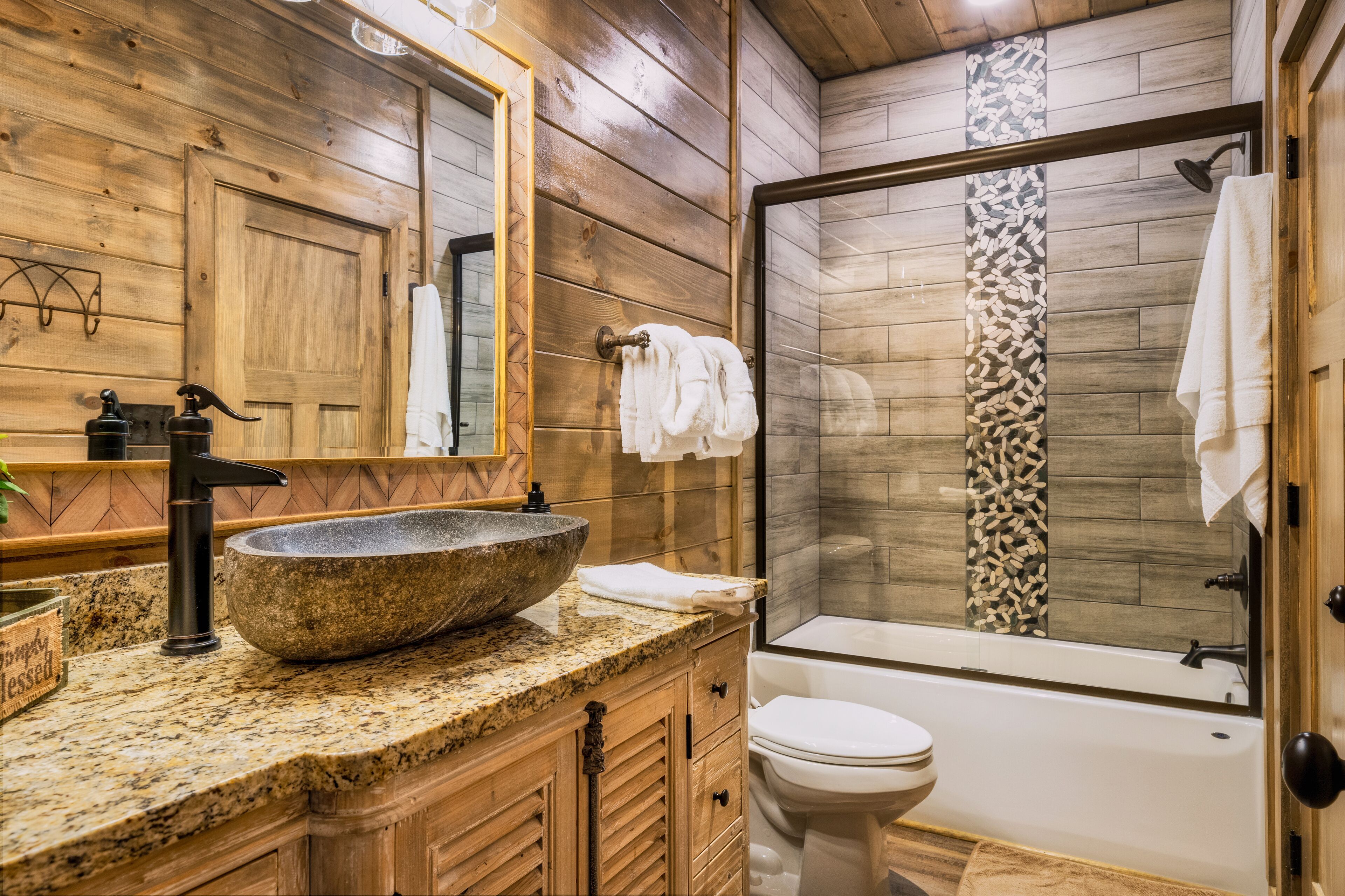 Un baño estilo cabaña de madera con un lavamanos de piedra grande, un inodoro y una ducha con cortina de estampado de leopardo.
