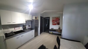 Una cocina compacta con armarios blancos, un microondas, un refrigerador y una cafetera.