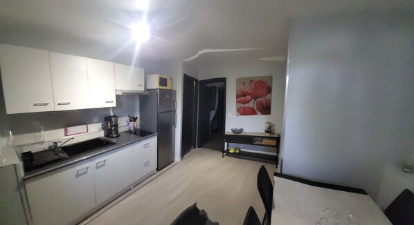 A compact kitchen with white cabinets, a microwave, a refrigerator, and a coffee maker.