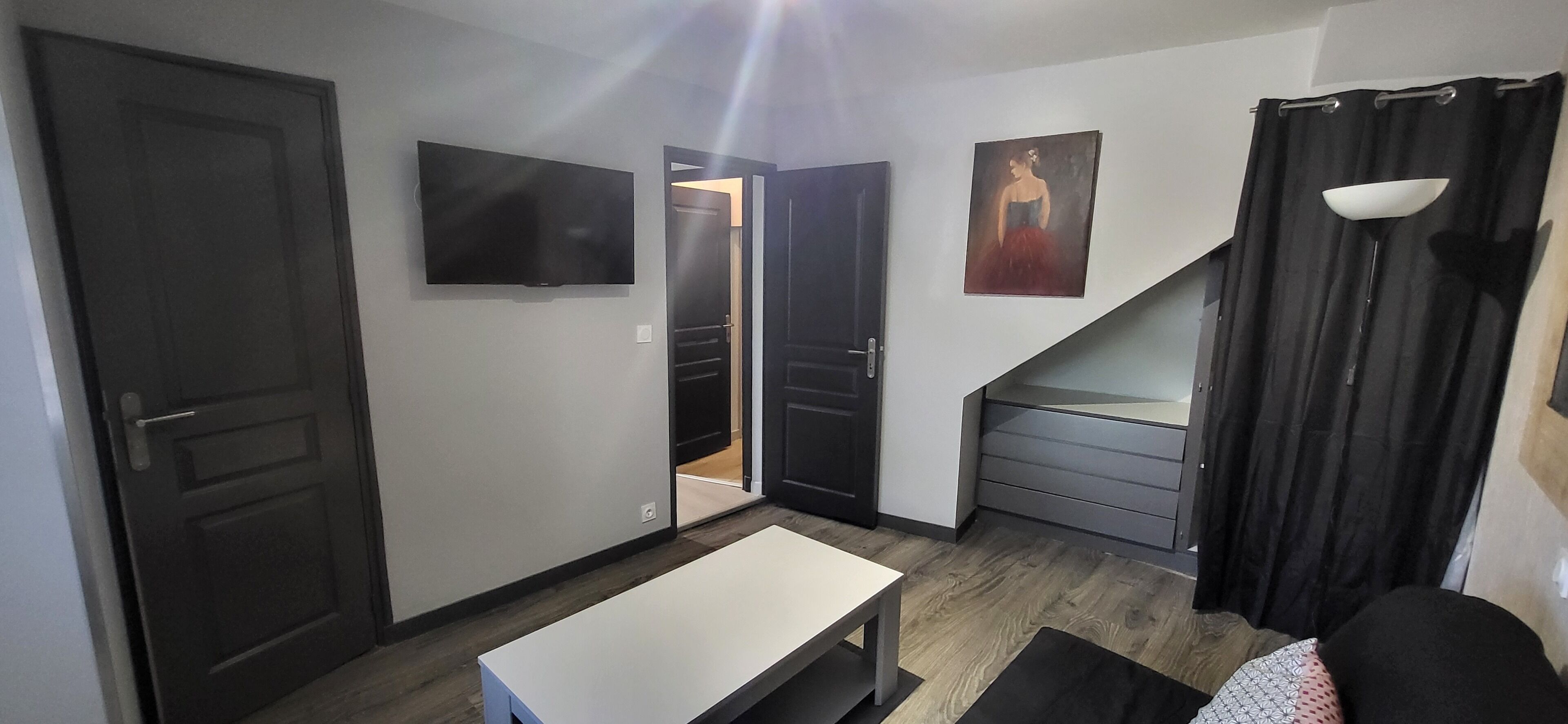 Una habitación con televisor, un cuadro, una escalera y una puerta que da a otra estancia.