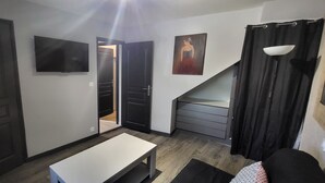 Una habitación con televisor, un cuadro, una escalera y una puerta que da a otra estancia.