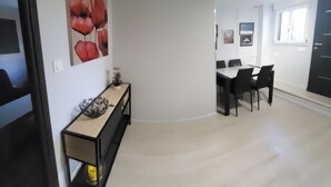 Una sala de estar moderna con comedor, que incluye un cuadro grande, una mesa consola con adornos y una mesa de comedor con sillas.