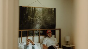 A bedroom with a bed, a ceiling fan, a nightstand, and a wall-mounted painting.