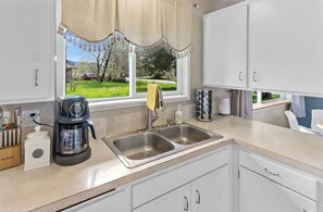 Enjoy a bright kitchen with a double sink and coffee maker, offering a view of the surrounding green landscape.