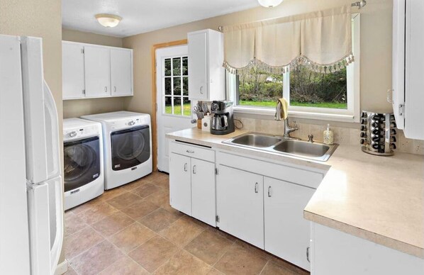Compact kitchen with refrigerator, washing machine, coffee maker, and sink, offering ample storage and a view of the surrounding greenery.