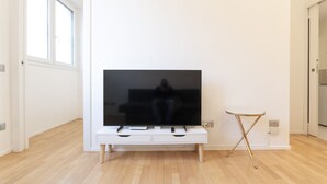 Ein modernes Wohnzimmer mit einem Flachbildfernseher auf einer weißen Konsole, Holzboden und einem kleinen Beistelltisch.