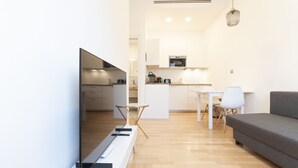 Ein modernes Wohnzimmer mit Flachbildfernseher, einem grauen Sofa und einem Essbereich mit weißem Tisch und Stühlen.