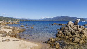 Un littoral rocheux bordé d’une eau d’un bleu limpide, avec des montagnes qui se dessinent à l’horizon.