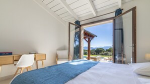 Une chambre à coucher avec un lit, un bureau et une chaise. Une grande fenêtre offre une vue sur l’extérieur.