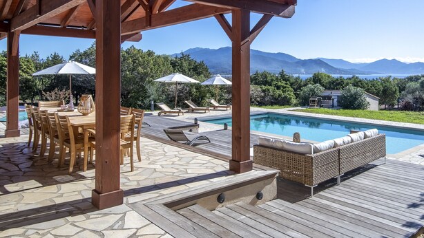 Une terrasse en bois avec une piscine, des chaises longues et une pergola.