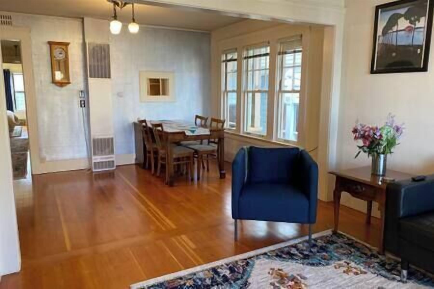 A spacious living area with a dining table, chairs, a blue armchair, and a rug.