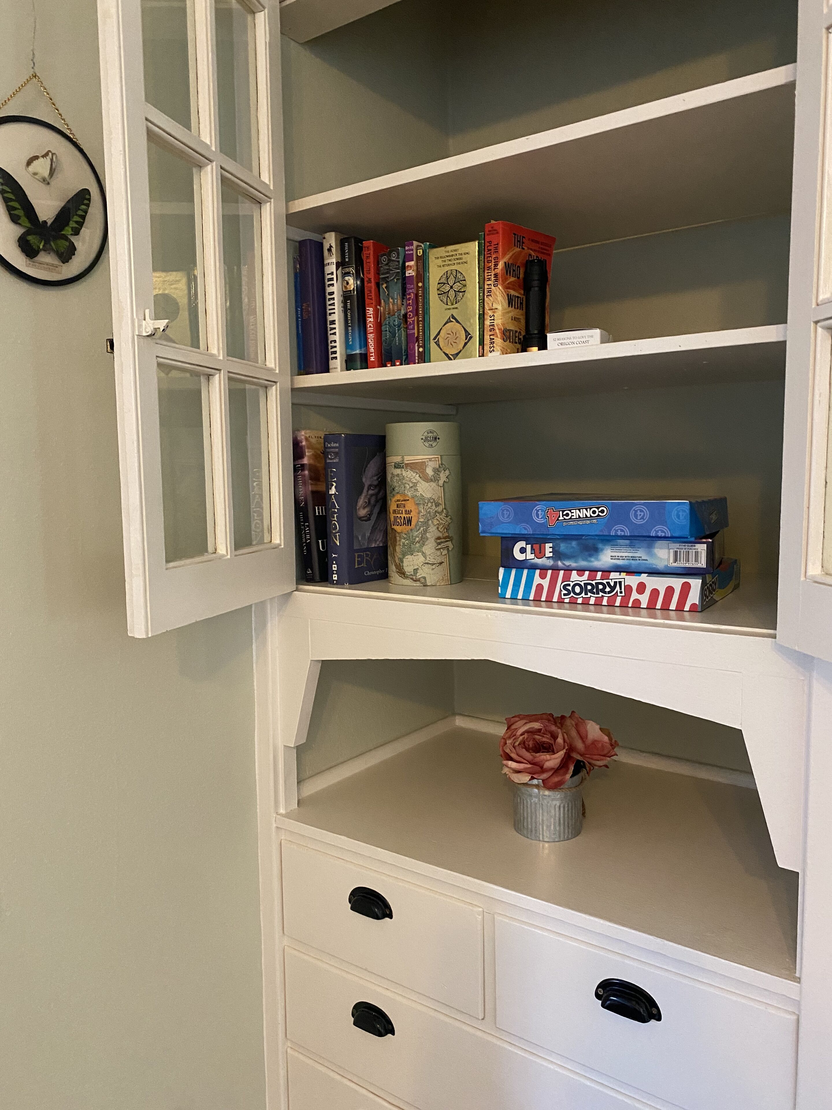 A bookshelf with various books, a jigsaw puzzle, and a Clue game box.