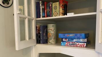 A bookshelf with various books, a jigsaw puzzle, and a Clue game box.