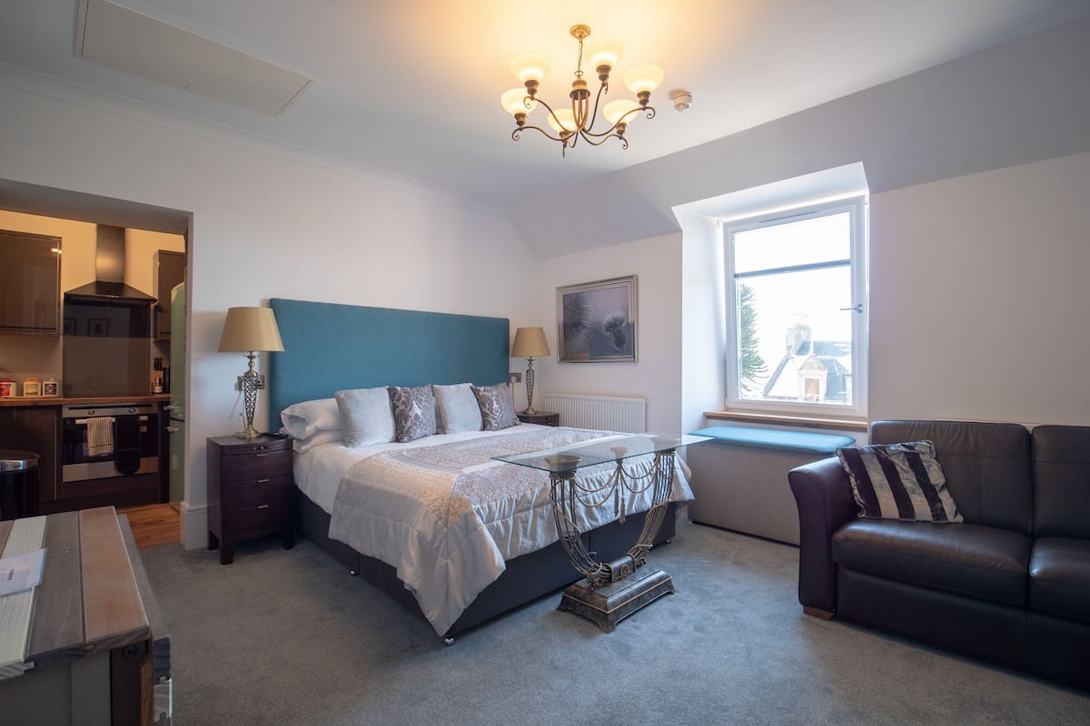 Une chambre avec un lit, une fenêtre, un canapé et un coin cuisine.