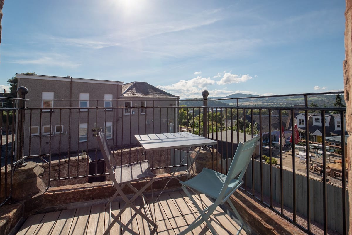 Un balcon avec une table et des chaises, donnant sur un quartier résidentiel et des montagnes.