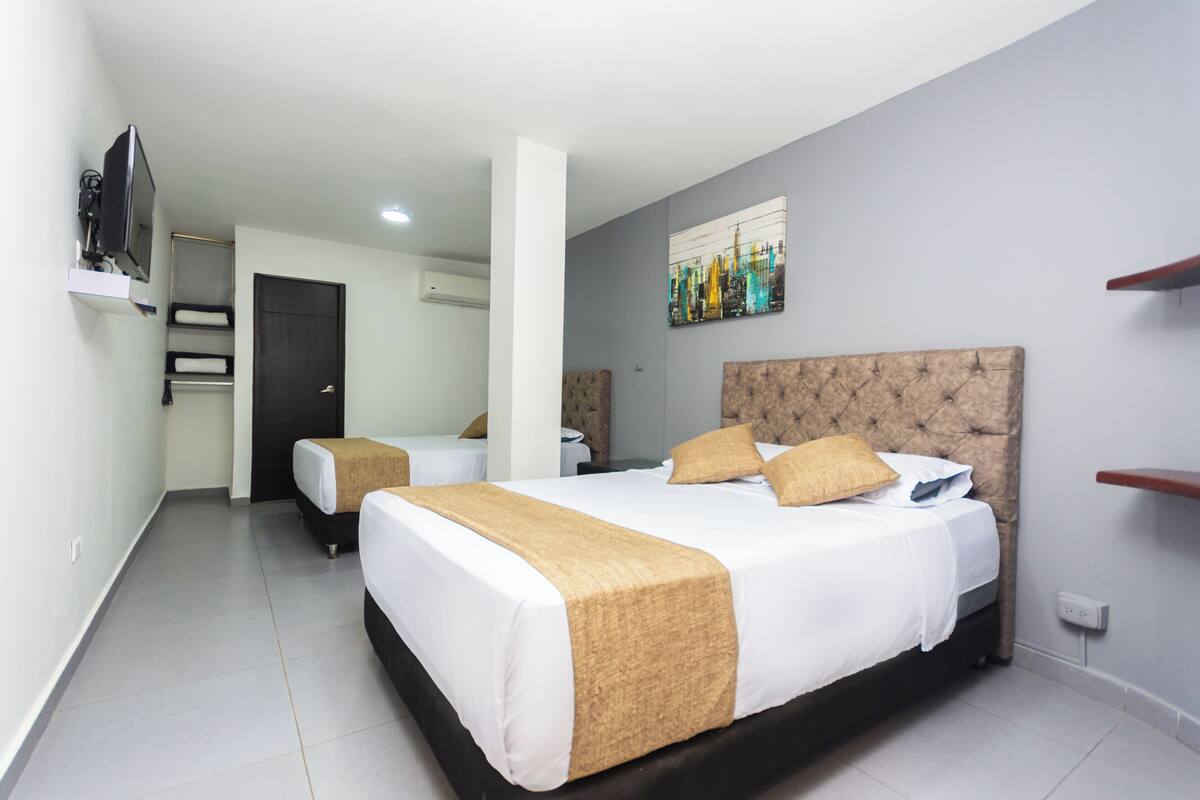 A hotel room with a large bed, a smaller bed, a TV, and a painting on the wall.