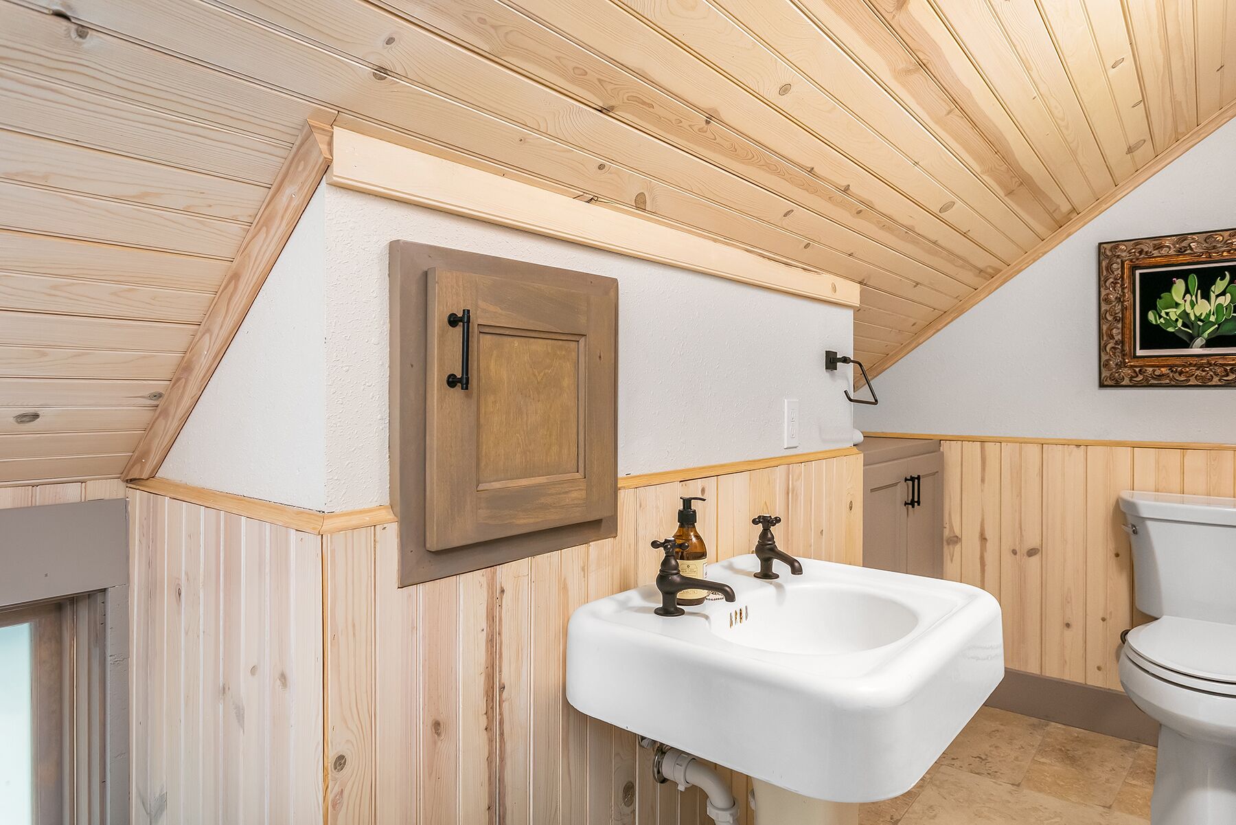 A bathroom with wooden paneling, a white sink with vintage-style faucets, and a wooden cabinet.