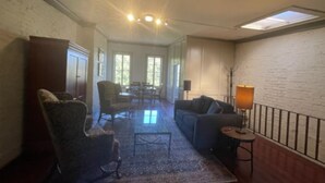 A spacious living room with a large rug, a sofa, and a chair. There is a dining area in the background with a table and chairs.