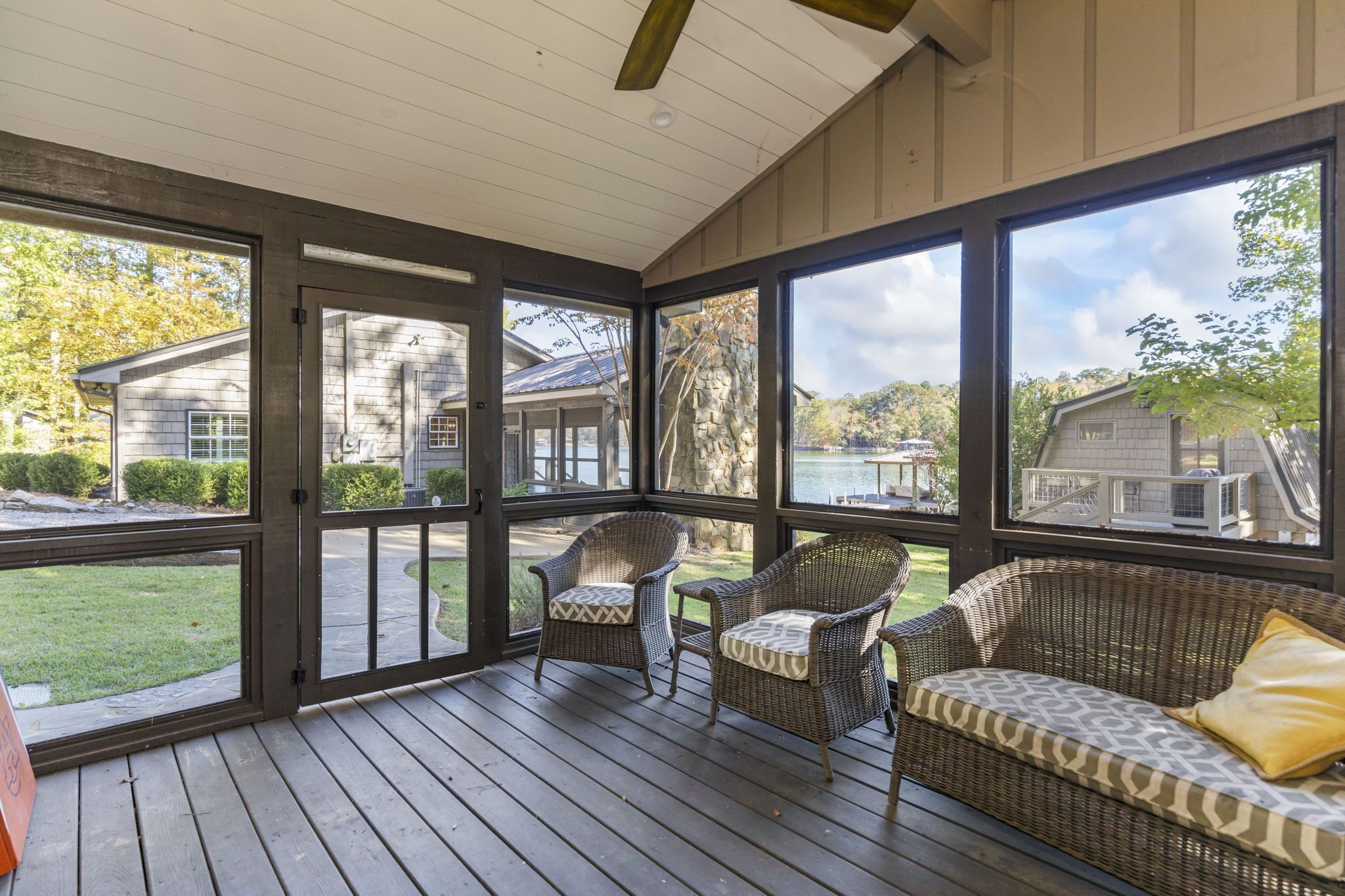 A covered porch with wicker furniture and large windows overlooking a residential area.