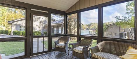 A covered porch with wicker furniture and large windows overlooking a residential area.