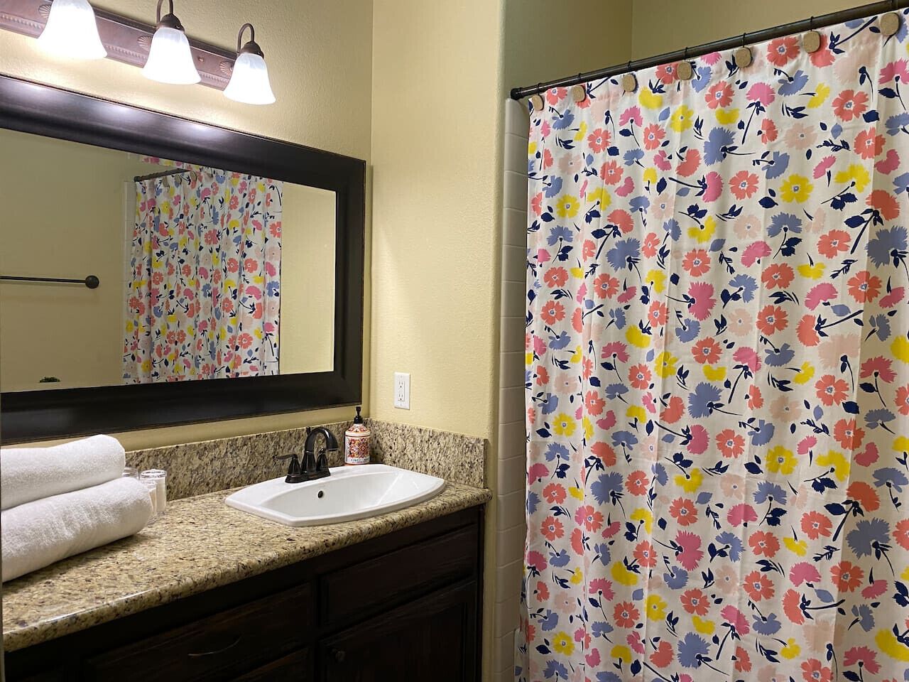 A bathroom with a sink, mirror, and floral shower curtain.